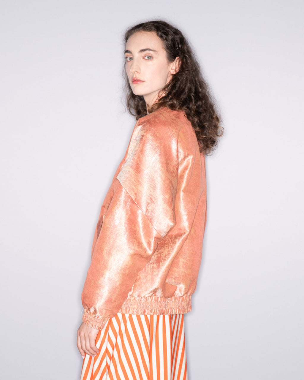 Woman wearing a peach jacket and striped skirt against a plain background